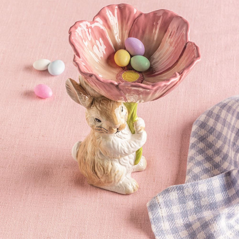 Ceramic bunny holding a pink flower candy dish with Easter eggs.