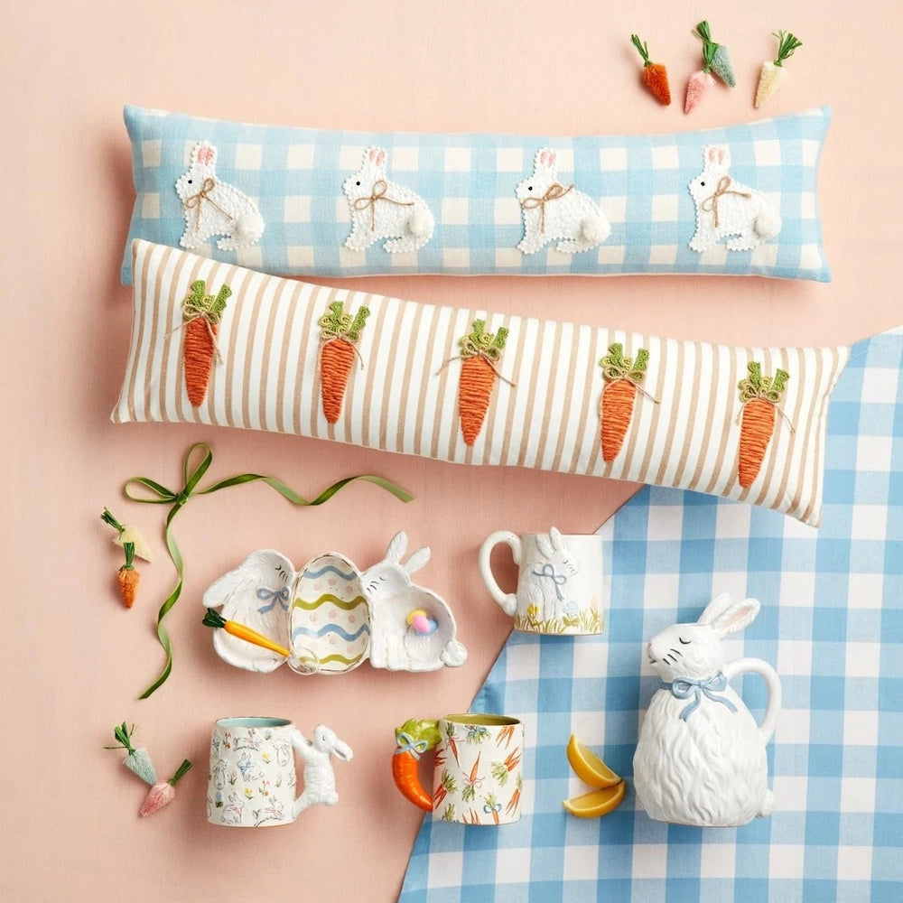 Easter-themed pillows, mugs, and bunny-shaped ceramics displayed on a pink and blue checkered background.