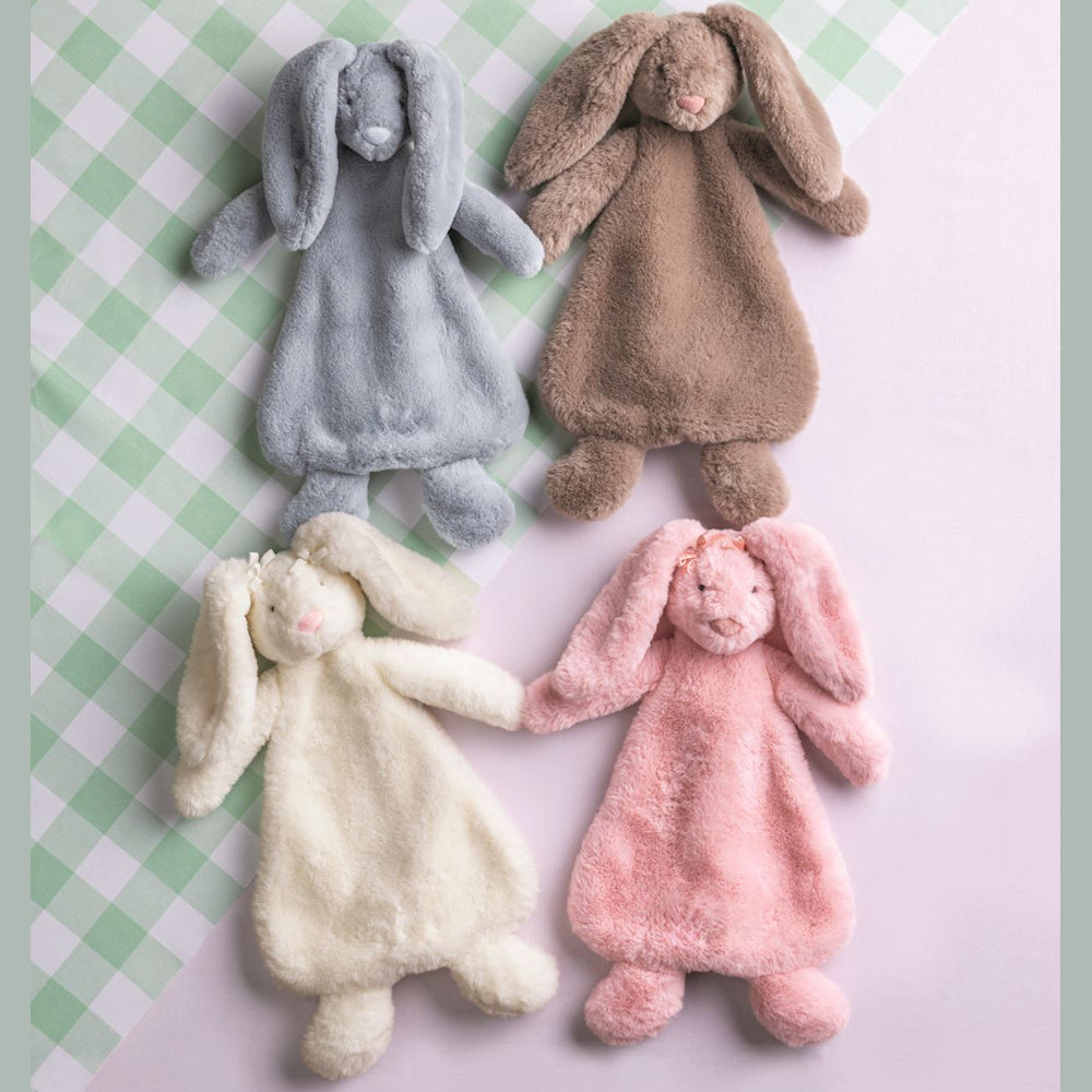 Four plush bunny lovey security blankets in blue, brown, cream, and pink colors on a green gingham and pink background.