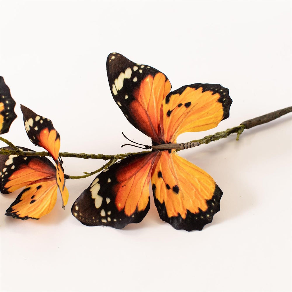 Close-up of decorative orange and black monarch butterflies attached to a faux textured branch.