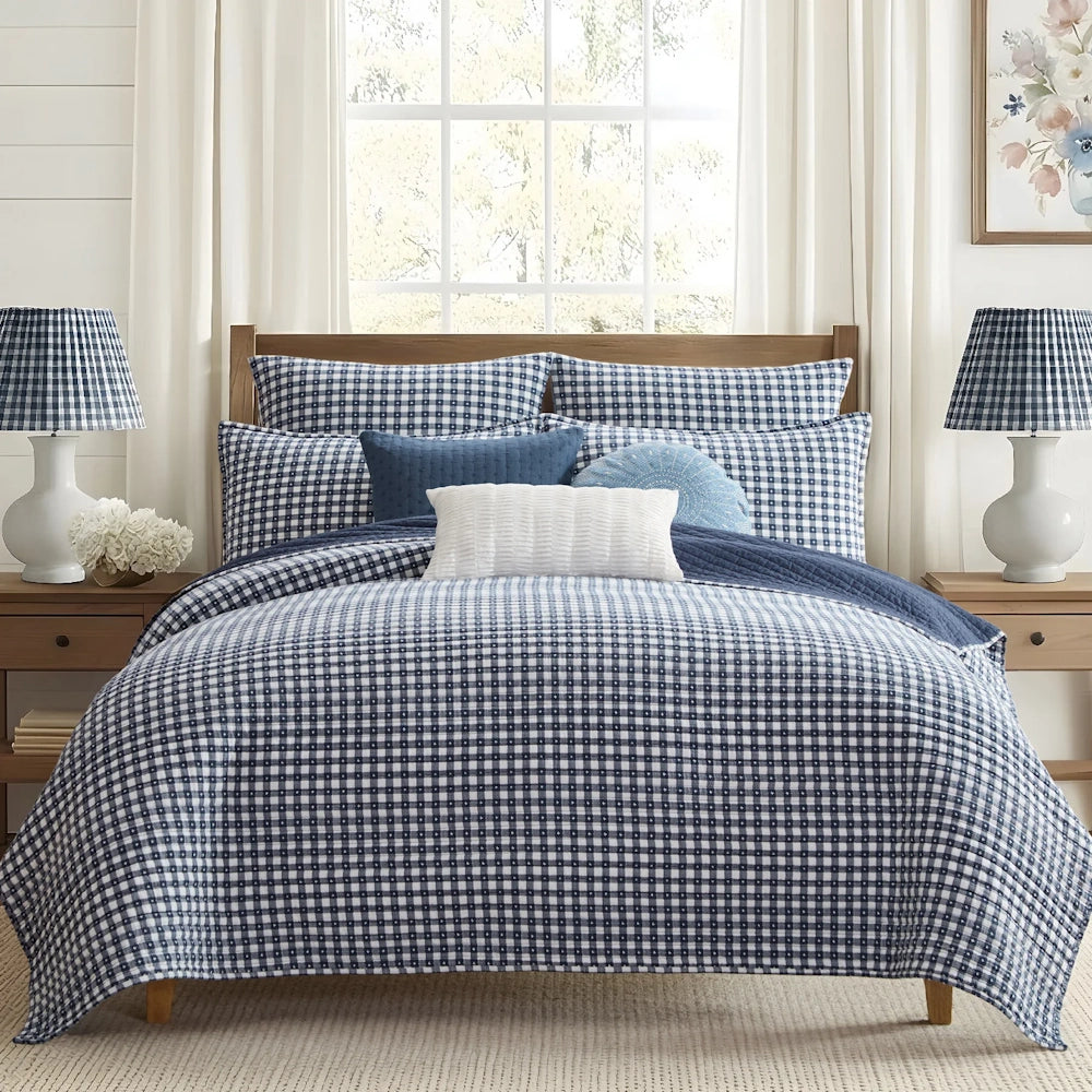 Navy and white gingham check quilt bedding set on a wooden bed with matching pillows and side lamps.