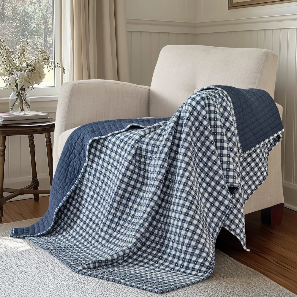 Navy blue and white gingham quilted throw blanket draped over an off-white armchair in a sunlit room.
