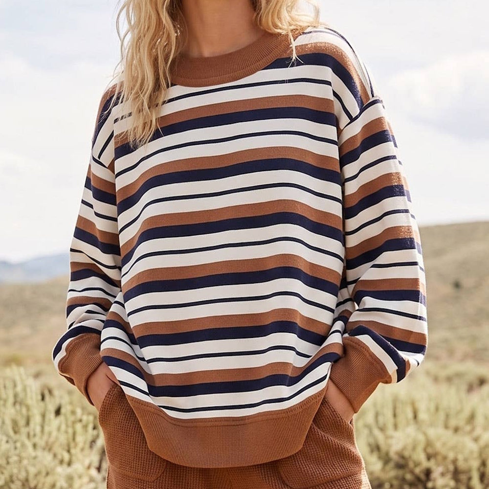 Person wearing an oversized, striped crewneck sweatshirt in camel brown, navy blue, and cream.