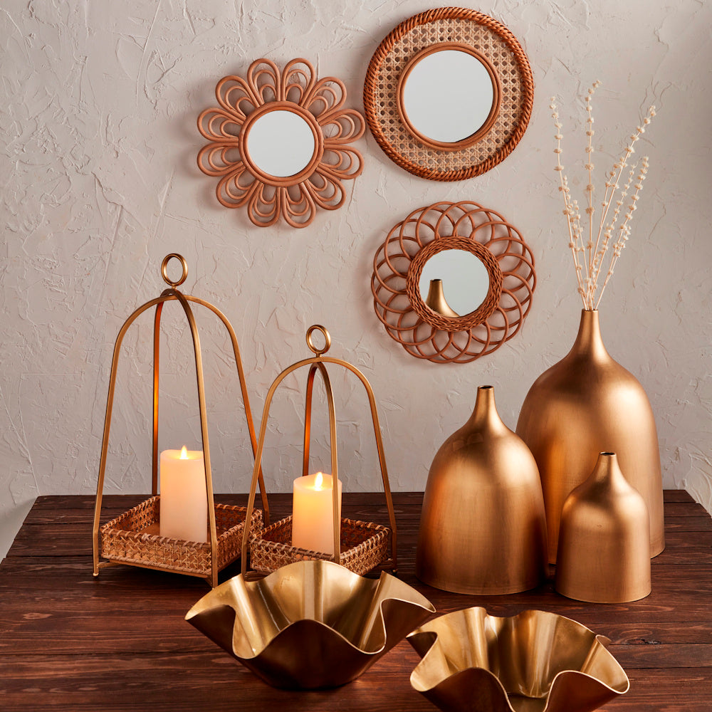 Gold lanterns with candles, metallic vases, and woven mirrors on a rustic wooden table for elegant home decor.
