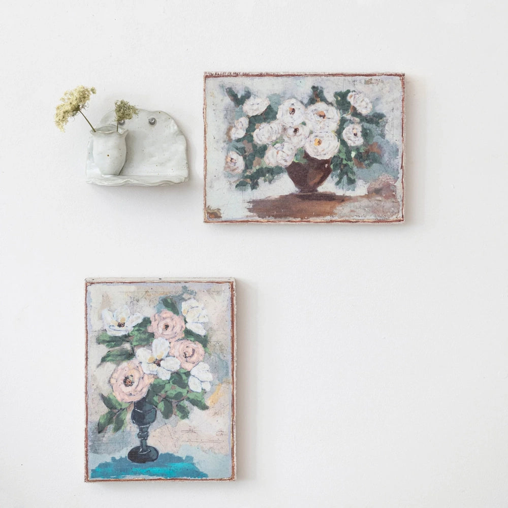 Vintage-style floral canvas wall art with white and pink flowers in vases and a small ceramic wall-mounted bud vase.