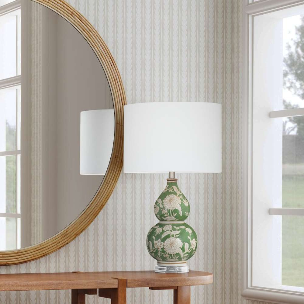 Green and white floral ceramic table lamp with white shade on a wooden console table next to a round mirror.