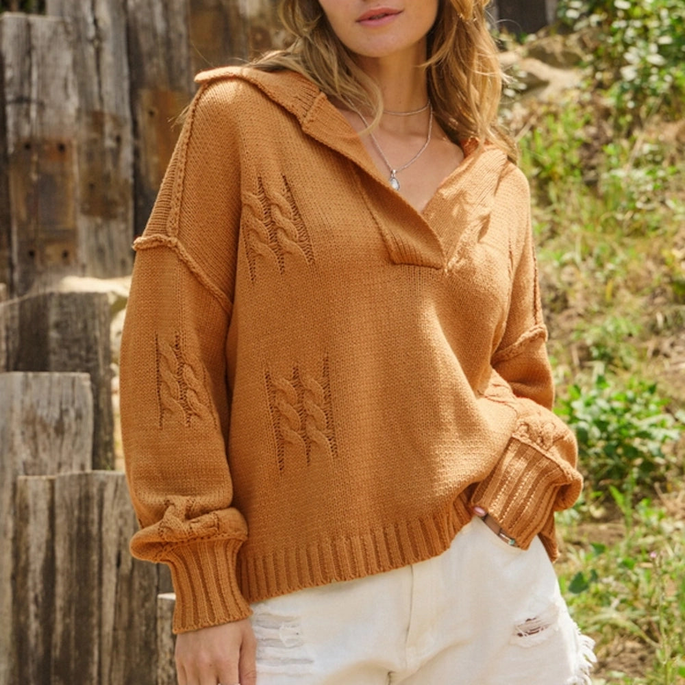 A woman wearing a caramel knit sweater with a wide collar, V-neck, and cable-knit panel details.