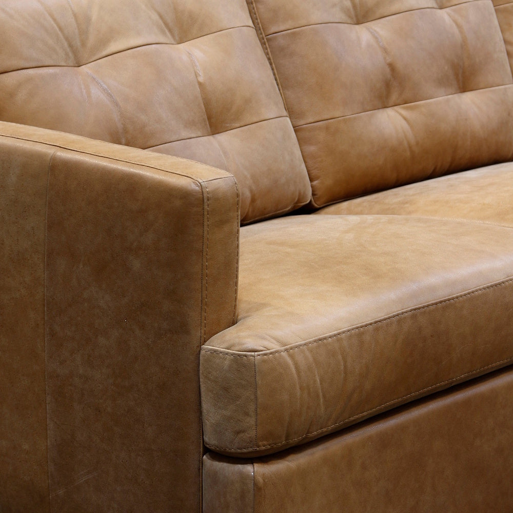Close up of caramel Italian leather sofa showcasing tufted back cushions, box arm and smooth seat cushion.