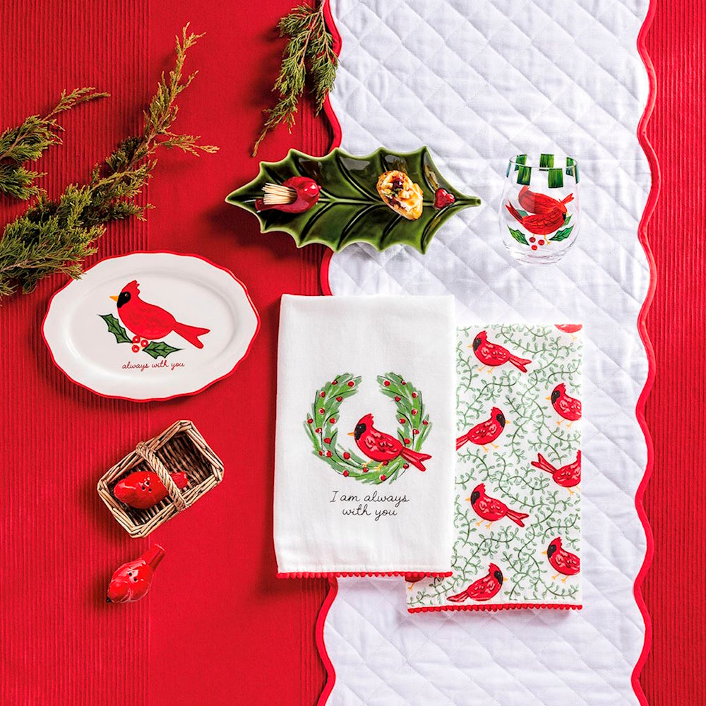 Holiday table setting featuring red cardinal towels, dishware, glass, and festive decor.