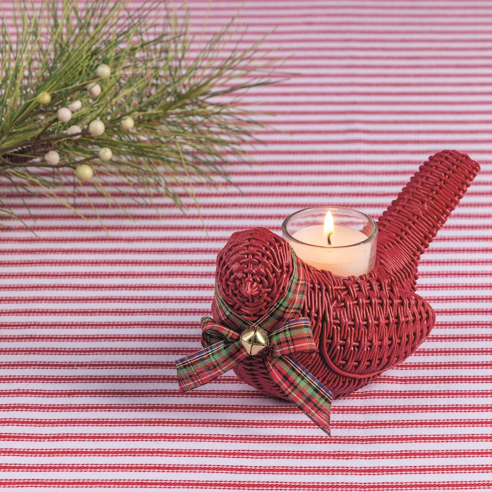 Red wicker cardinal votive holder with a lit candle, placed on a red and white striped table runner.