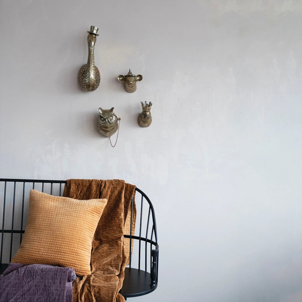 Gold cast aluminum animal head wall decor featuring an owl, swan, and cow above a black metal bench with textured pillows.