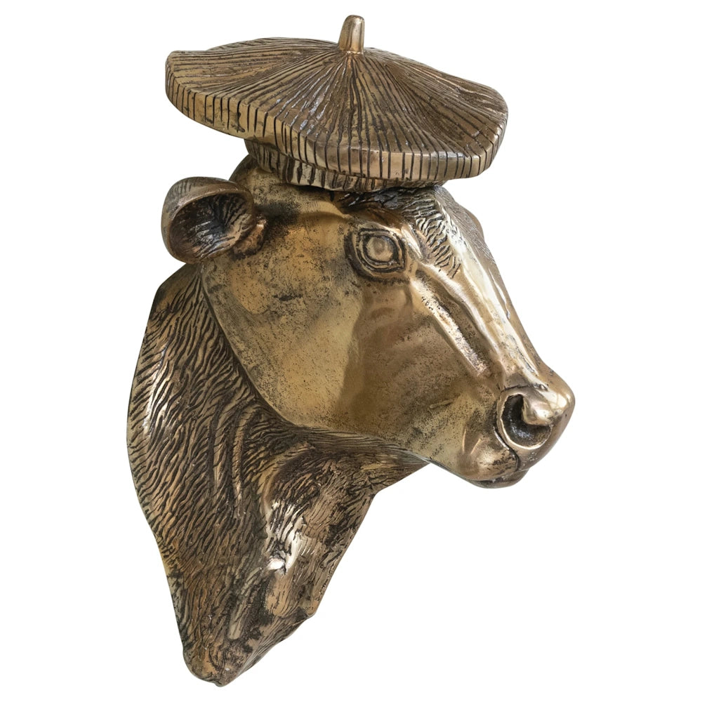 Side profile of a bronze metallic cow head wall decor wearing a textured beret, against a white background.