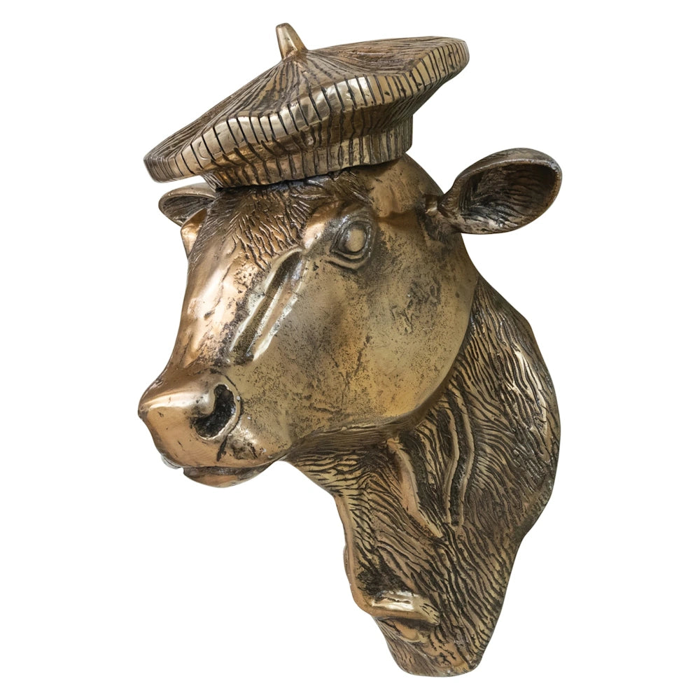 A bronze metallic cow head wall decor wearing a textured beret hat, isolated on a white background.