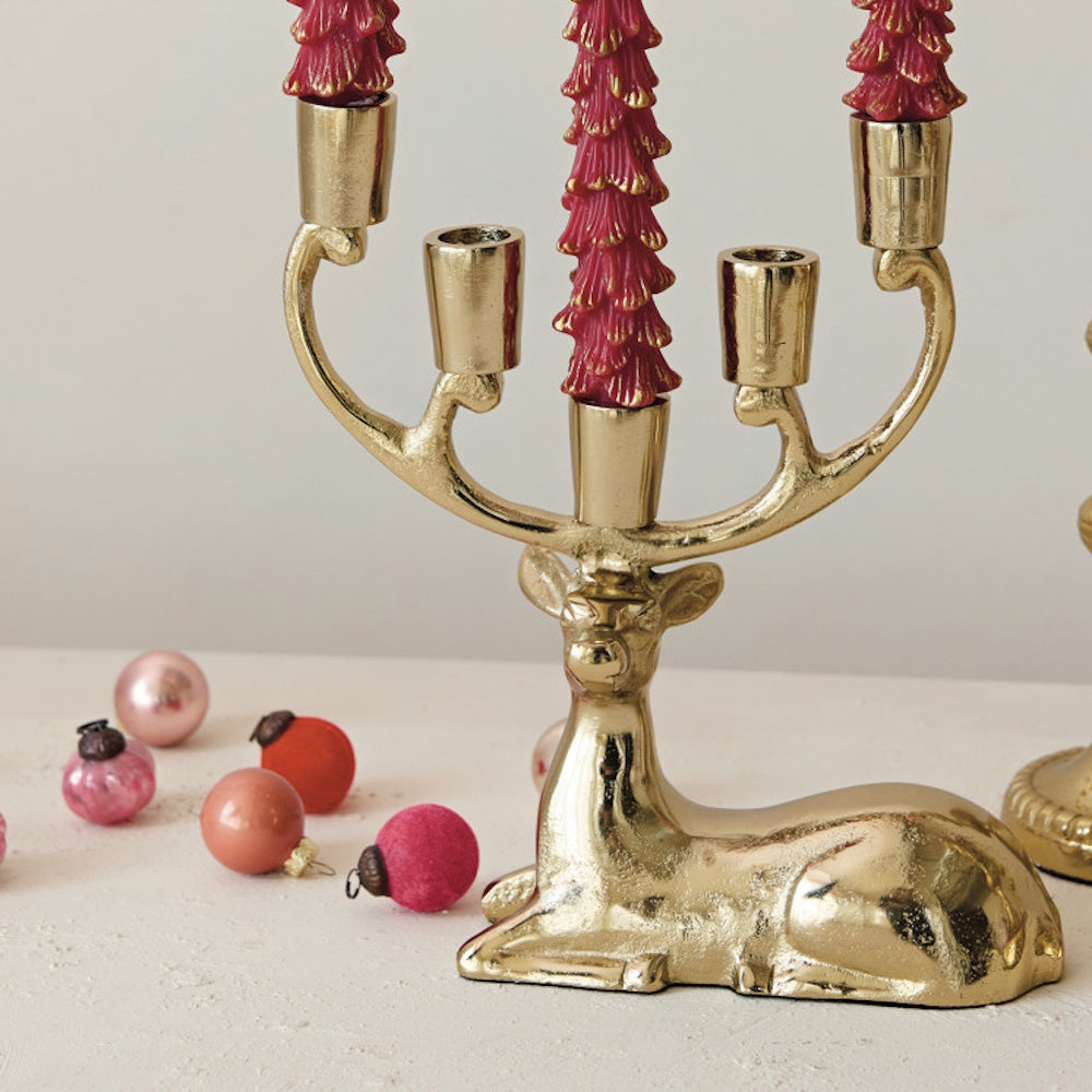 Gold deer candelabra holding red candles, surrounded by miniature decorative ornaments.