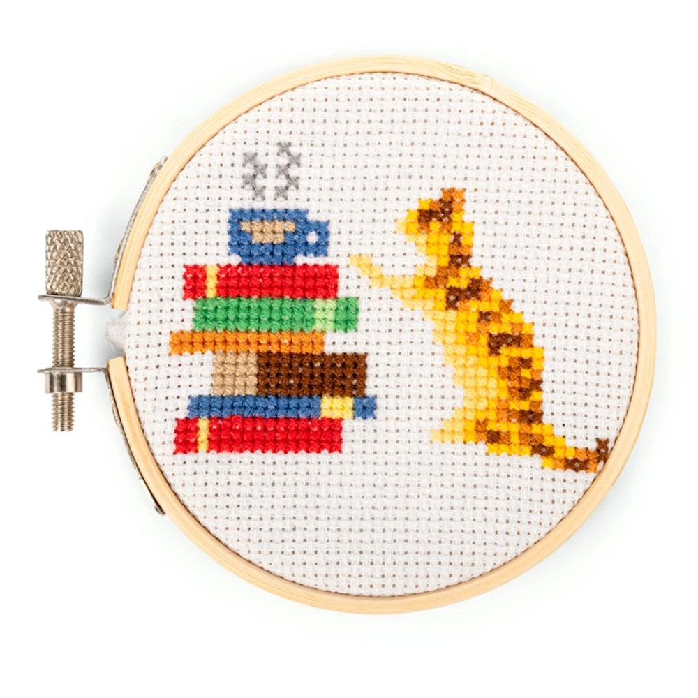 Mini cross-stitch kit featuring an orange tabby cat next to a stack of books and a steaming coffee cup in a wooden hoop.