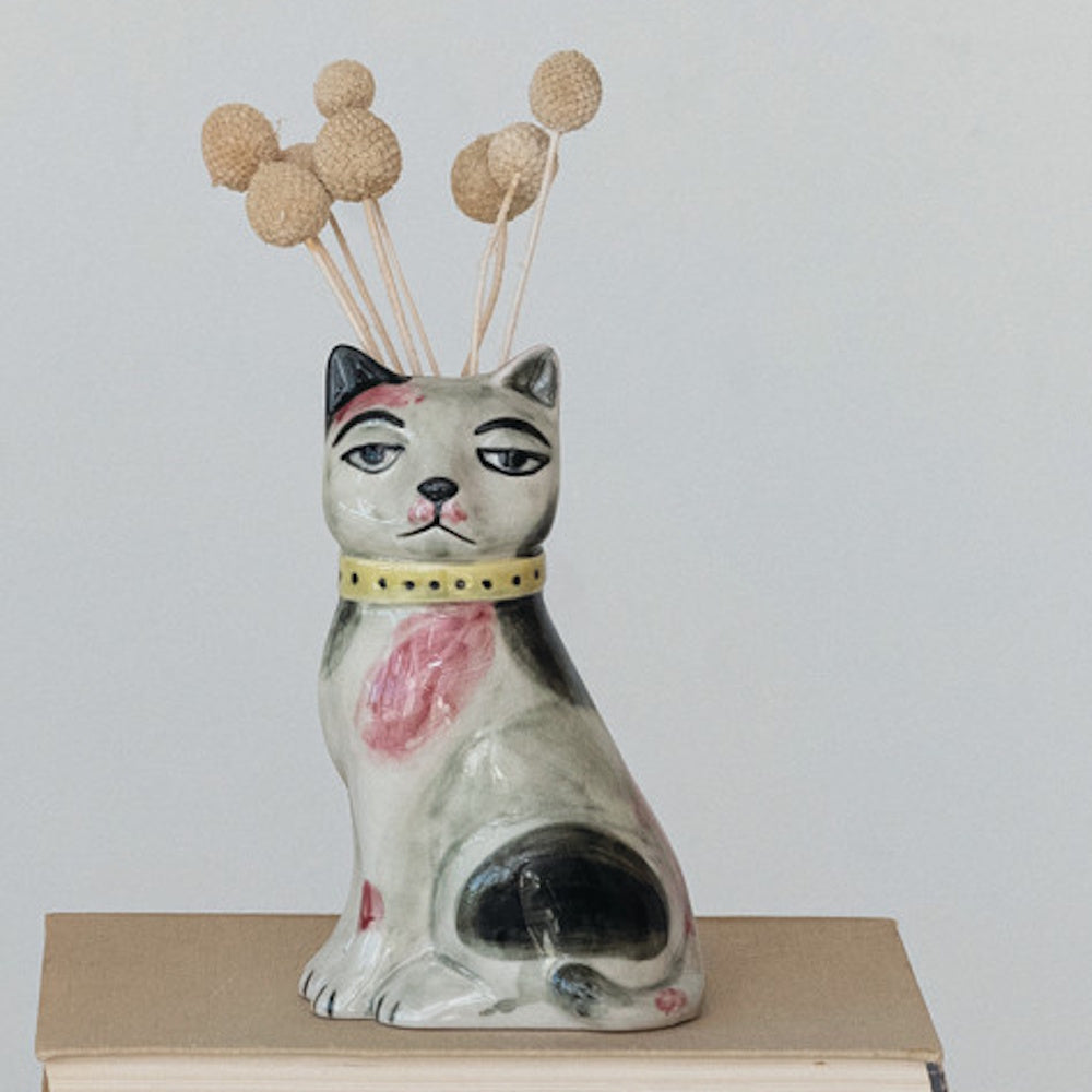Cat-shaped ceramic planter holding dried Billy Balls, sitting on a book against a plain background.