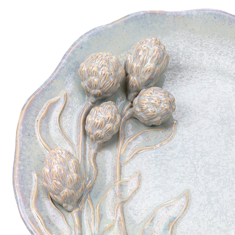 Close-up of a pale green ceramic platter featuring raised, 3D artichoke floral details and a crackle glaze finish.