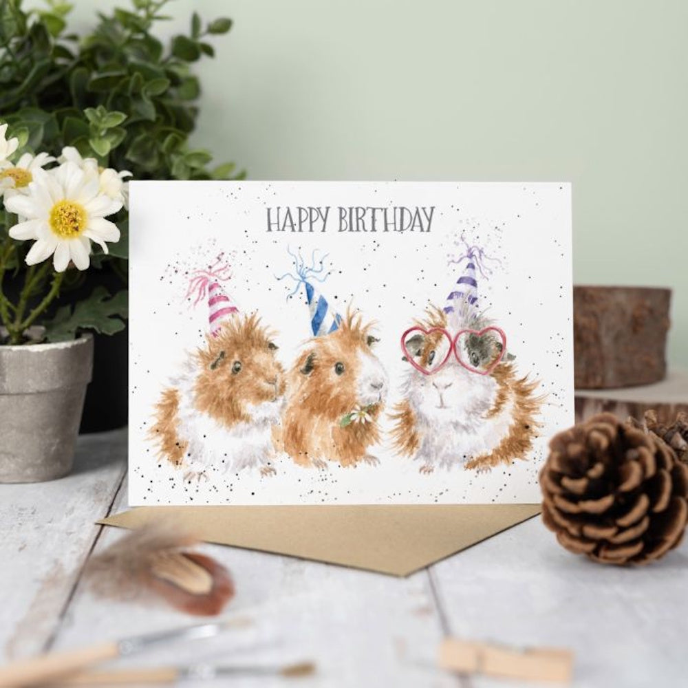 Watercolor guinea pigs in party hats and heart glasses on a "Happy Birthday" card with a brown envelope.