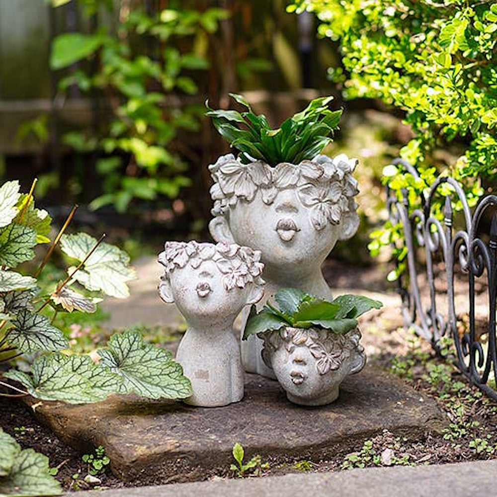 Three stone-look face planters with pouting lips displayed outdoors among garden plants.
