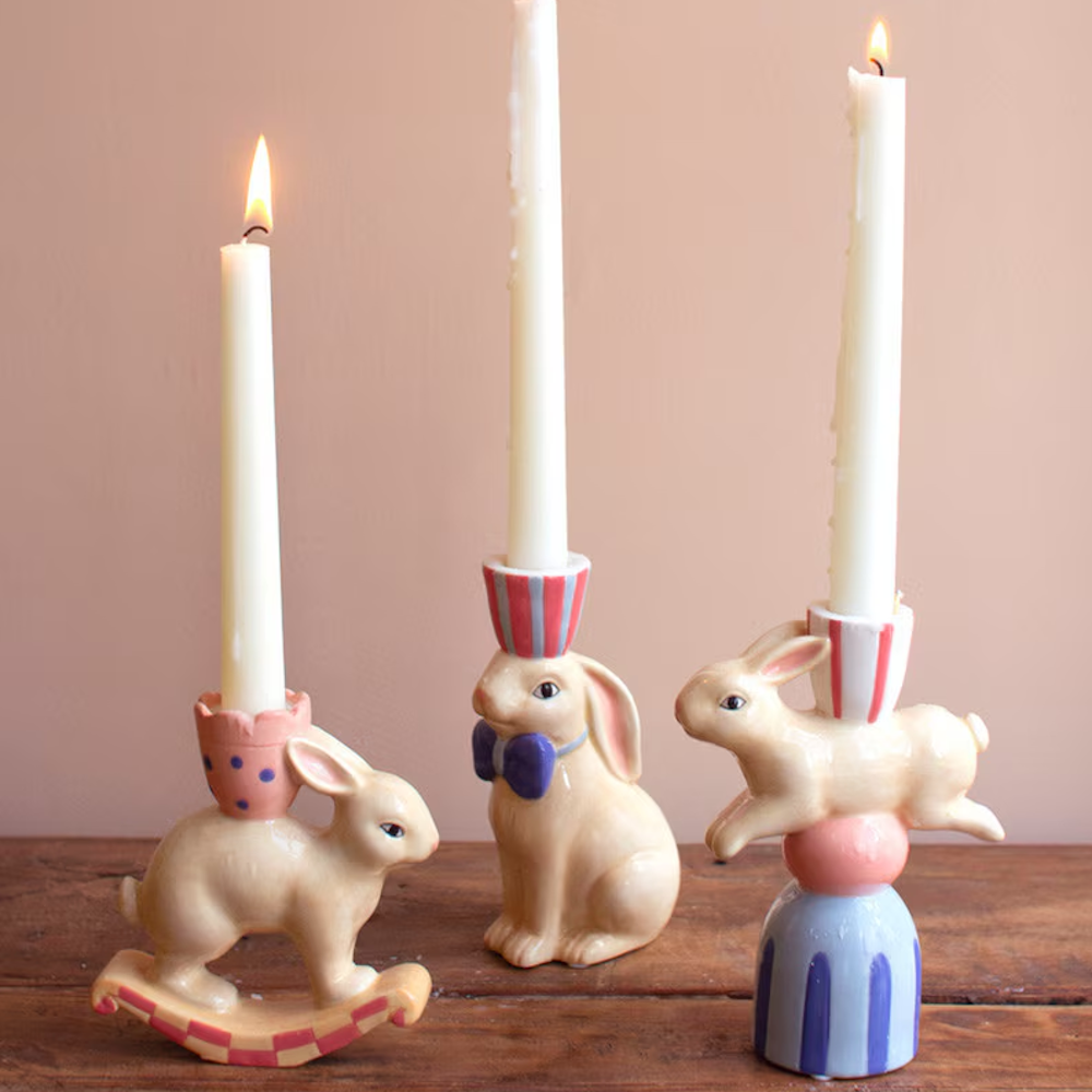 Whimsical ceramic bunny taper candle holders with lit white candles on a wooden surface for festive Easter decor.