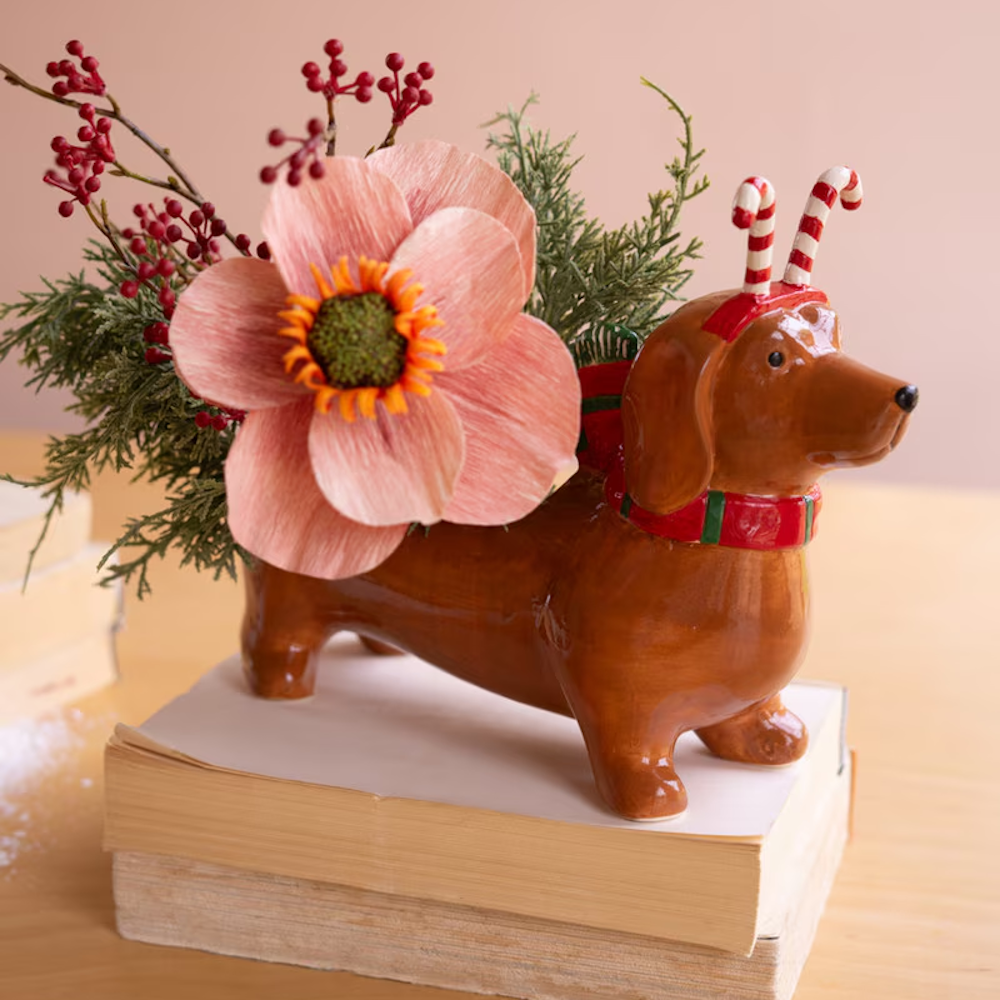 Ceramic dachshund planter with candy cane antlers and holiday greenery, resting on a stack of books.