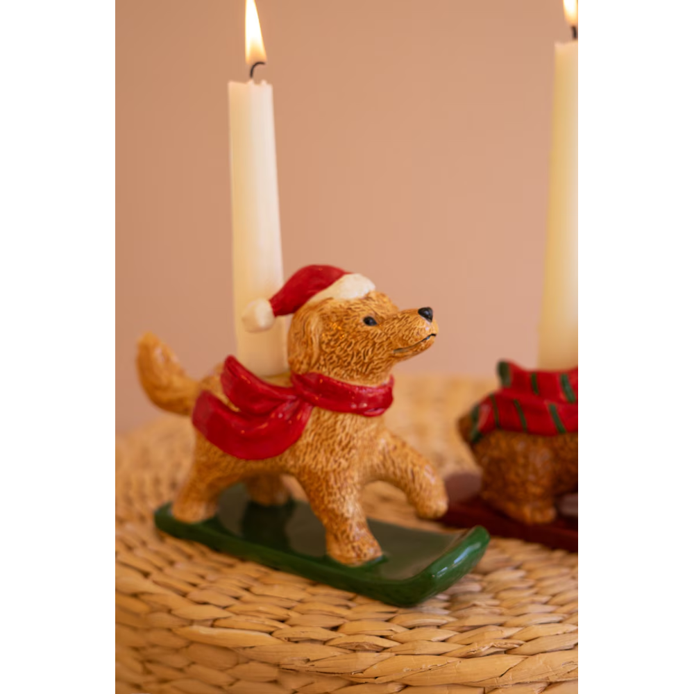 Close-up of a golden retriever dog taper candleholder wearing a Santa hat and red scarf on a sled.