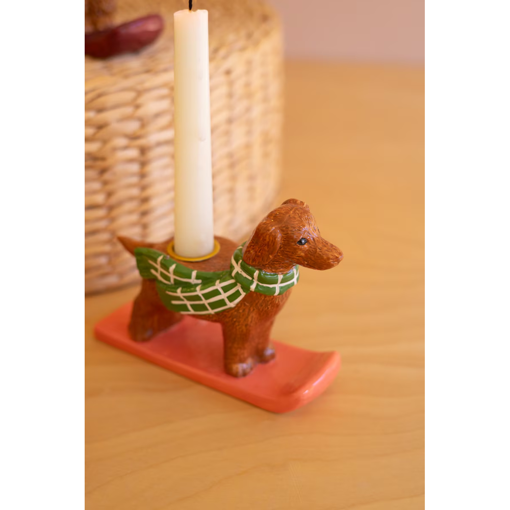 Close-up of a dachshund taper candleholder wearing a green plaid sweater on a coral sled.
