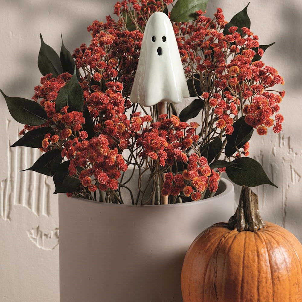 Ceramic ghost plant stake in a potted Halloween floral arrangement with orange flowers and a pumpkin.