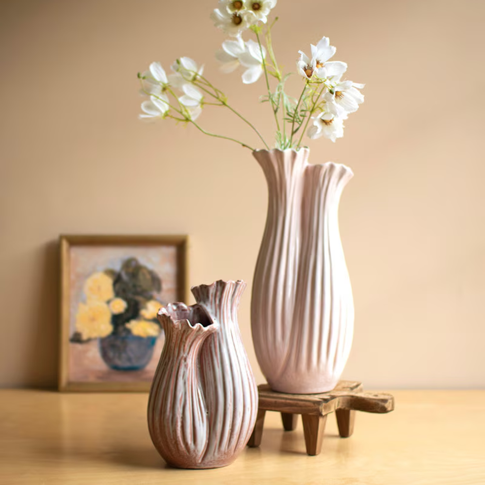 Two organic-shaped fluted ceramic vases in soft pink and beige tones with white flowers on a wooden table.