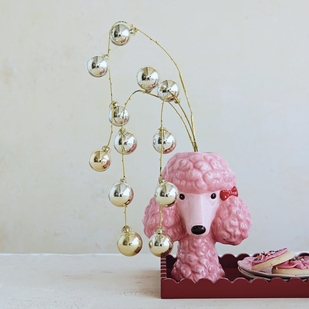 Pink ceramic poodle head vase holding silver ornament sprays on a decorated tray.