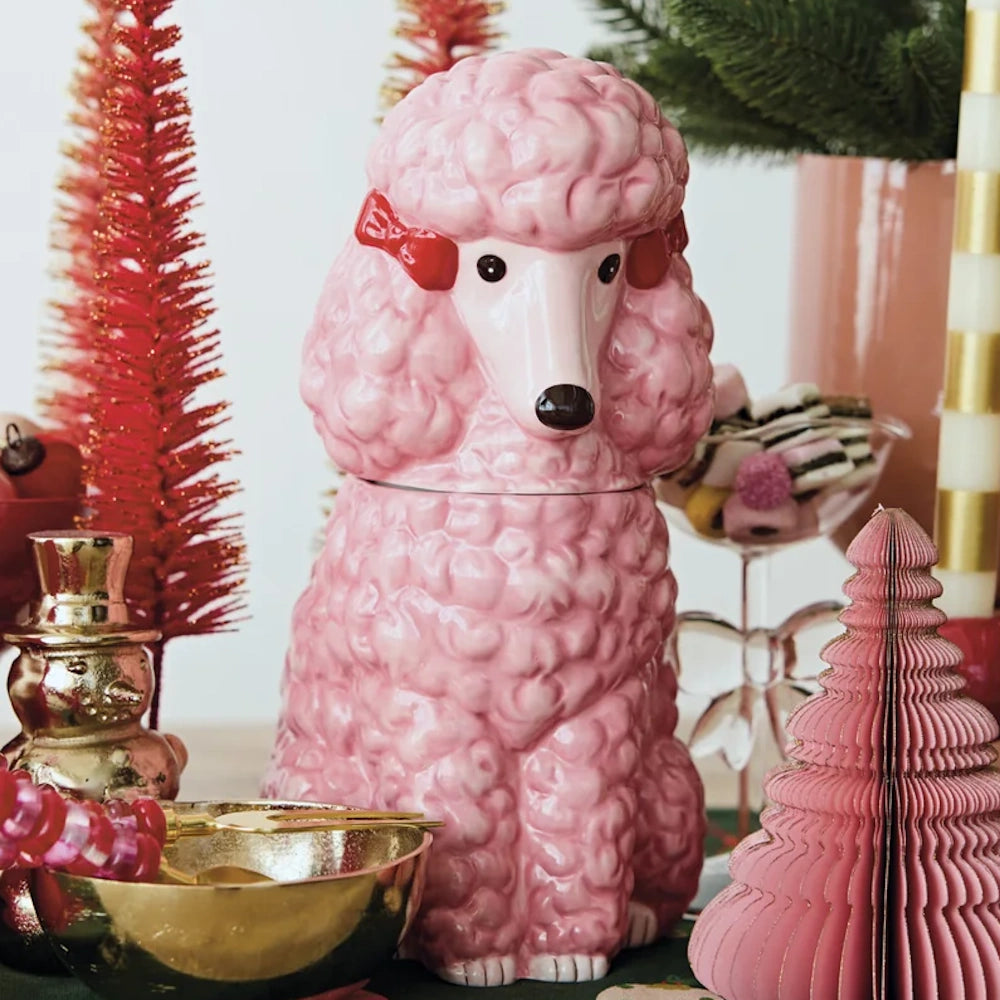 Pink ceramic poodle cookie jar with red bows, surrounded by holiday decor including small pink and red trees.