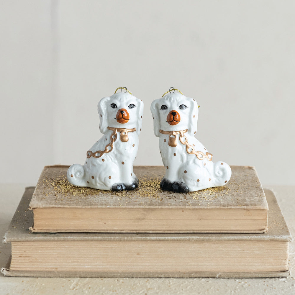 Pair of white ceramic Staffordshire dog ornaments with gold accents, sitting on stacked books.