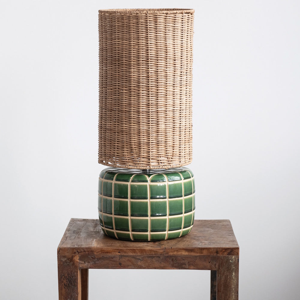 Green tiled ceramic table lamp with a hand-woven cylindrical rattan shade on a rustic wooden side table.