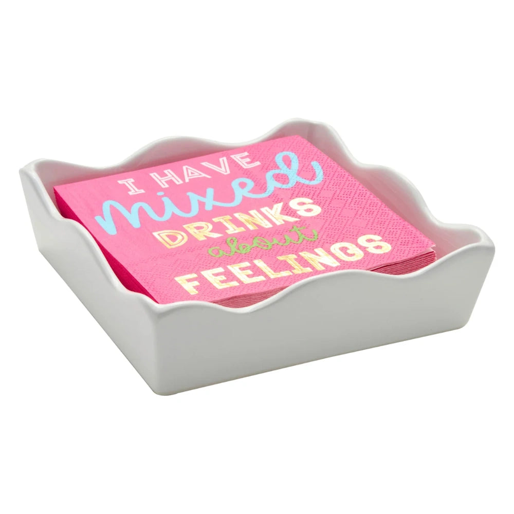 Side angle view of a white ceramic wave cocktail napkin tray holding pink napkins printed with I Have Mixed Drinks About Feelings text.