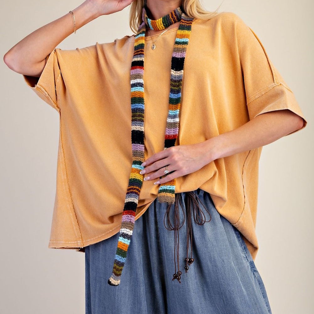 Oversized yellow short-sleeved knit top styled with a colorful striped skinny scarf and blue pants.