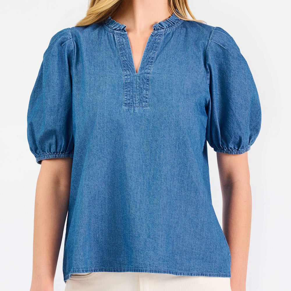 Woman wearing a blue chambray top with a ruffled v-neckline and puff short sleeves.