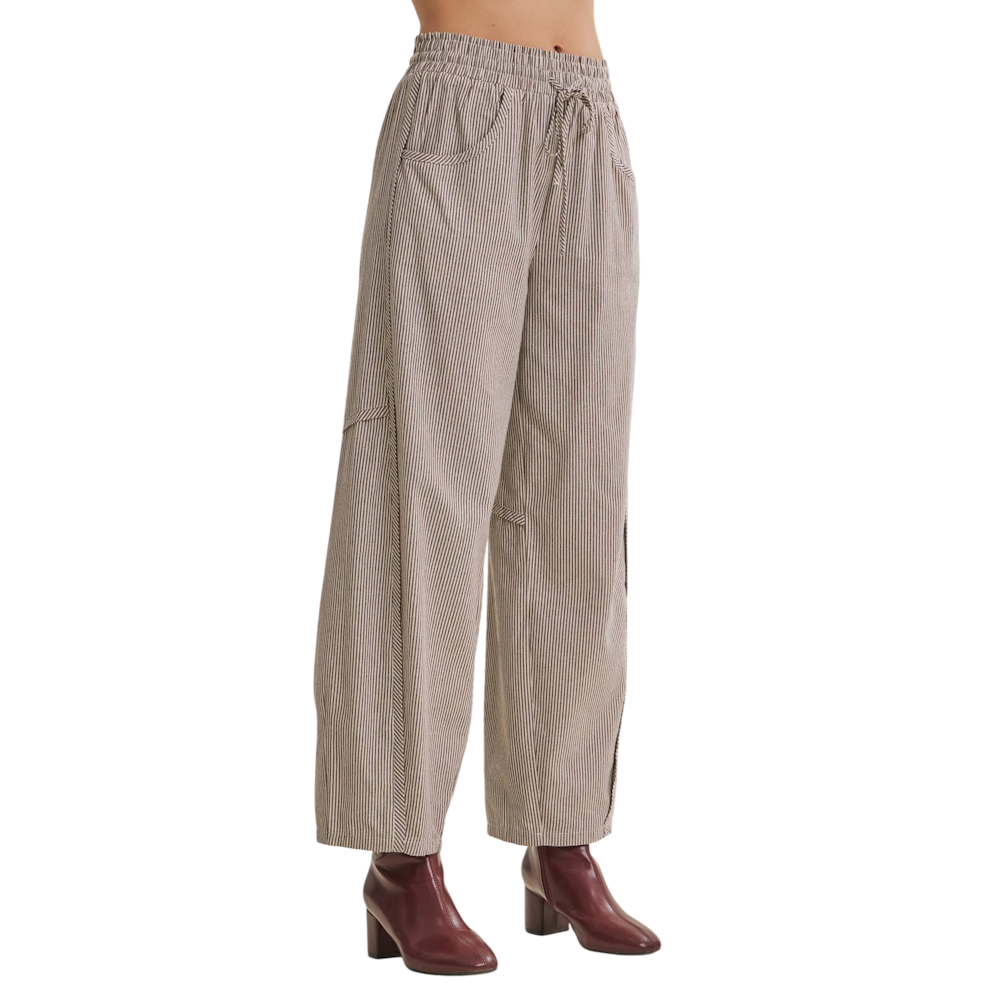 Side angle of model in brown pinstripe relaxed barrel pants with a drawstring waist and red heel boots.