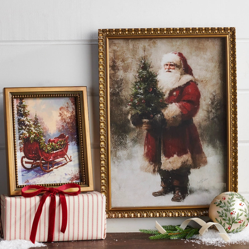 Two framed Christmas pictures, one of a sleigh in snow and one of Santa, displayed with a wrapped gift.