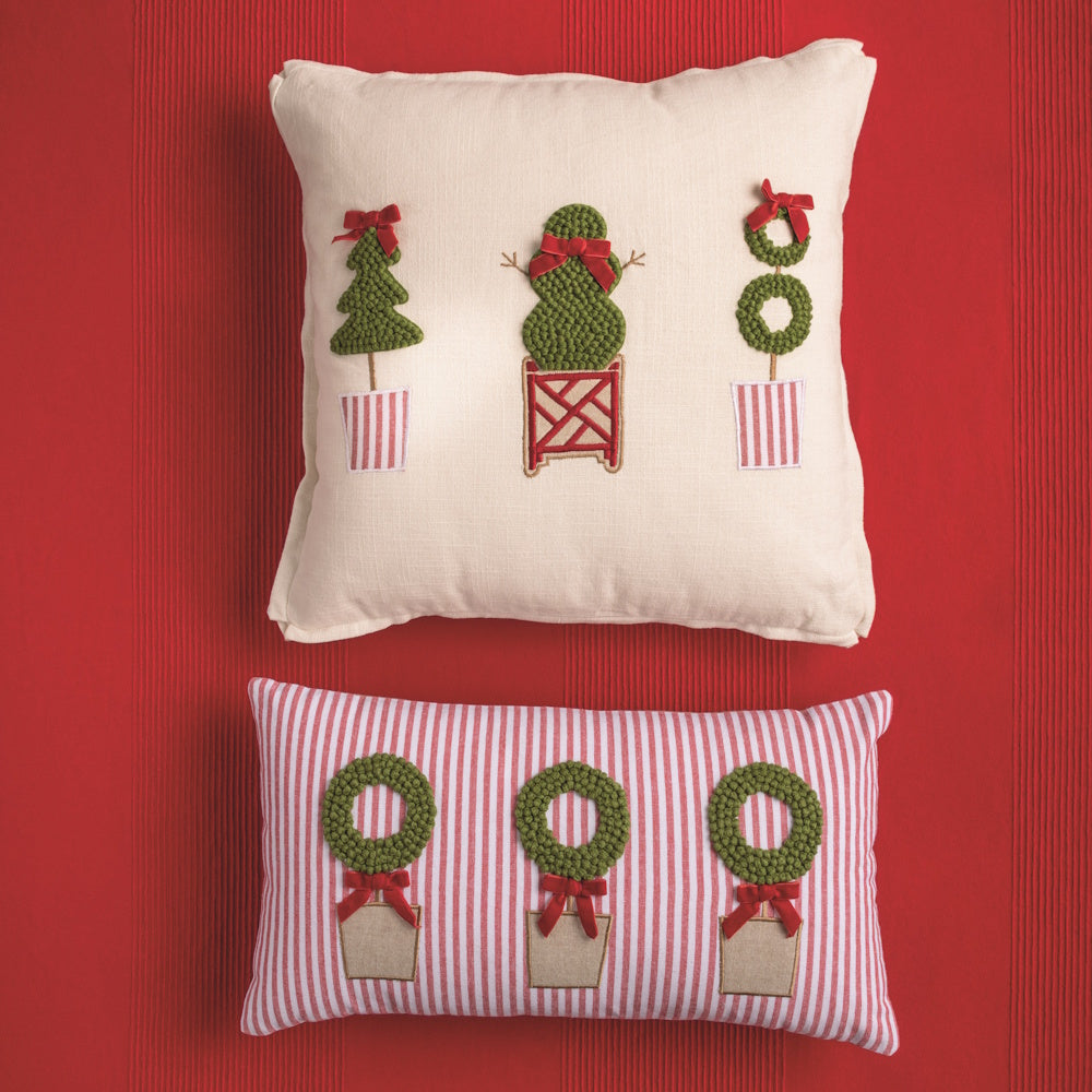 Two Christmas pillows featuring topiary designs, including a red-striped lumbar pillow with wreaths and a square white pillow with various topiary trees.
