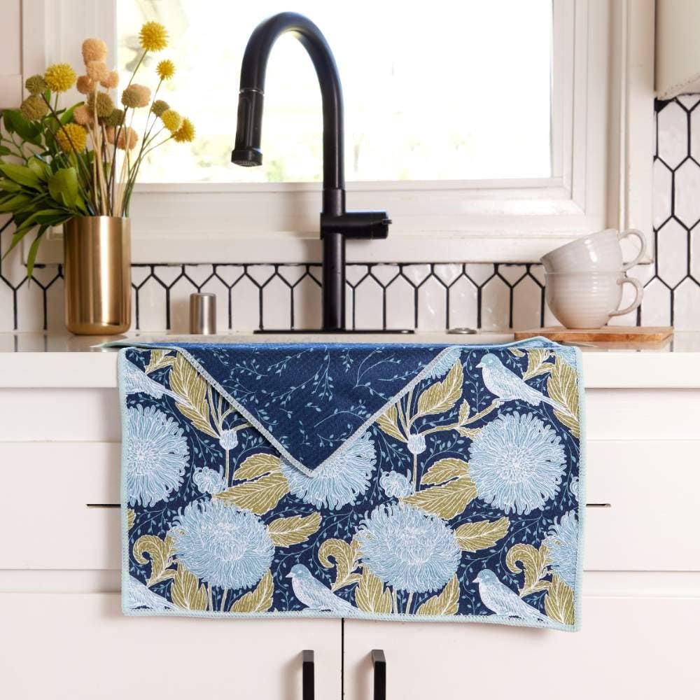 Blue floral tea towel with bird pattern draped over a white kitchen counter in front of a modern black sink.