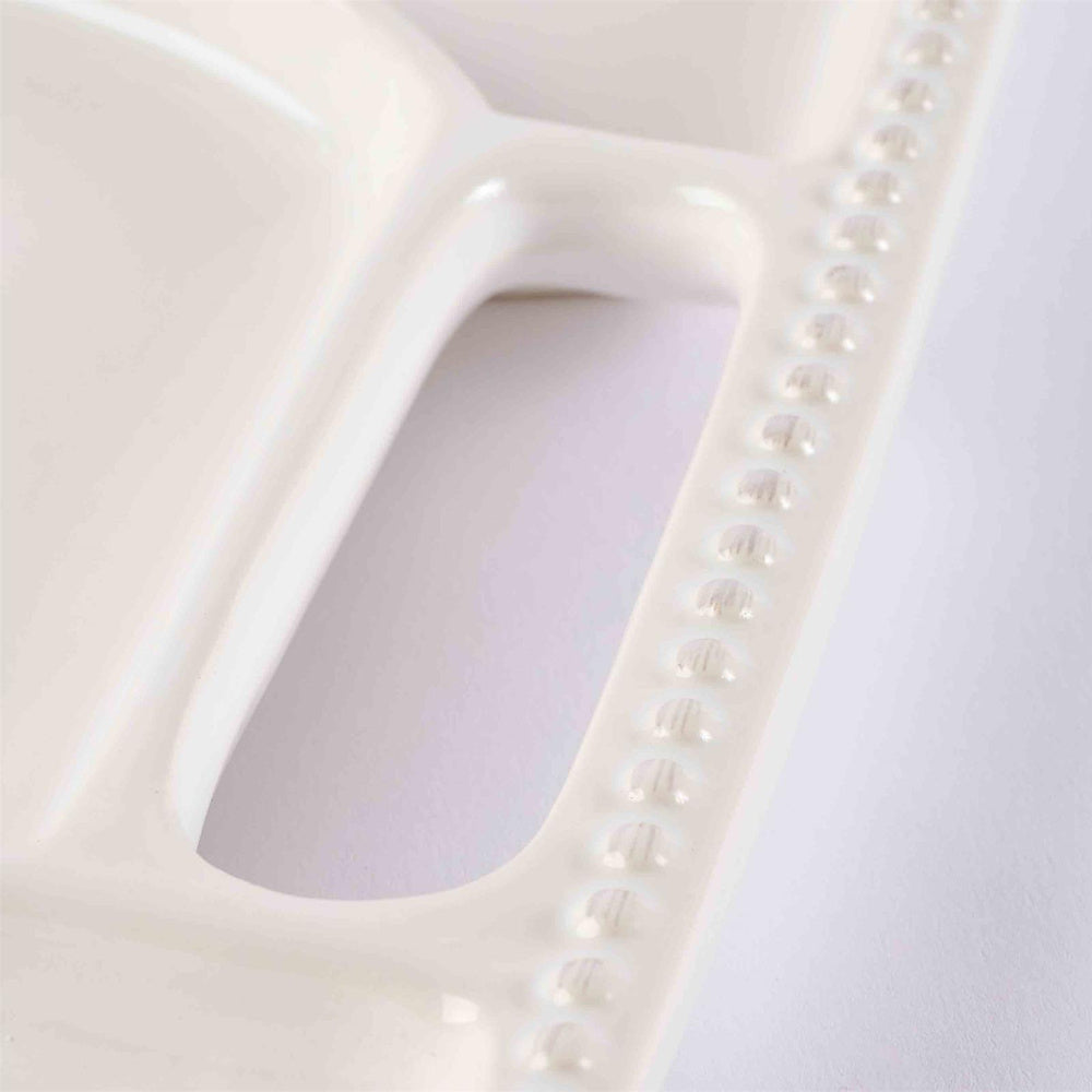 Close-up of a white ceramic charcuterie board featuring a beaded rim detail and divided serving compartments.