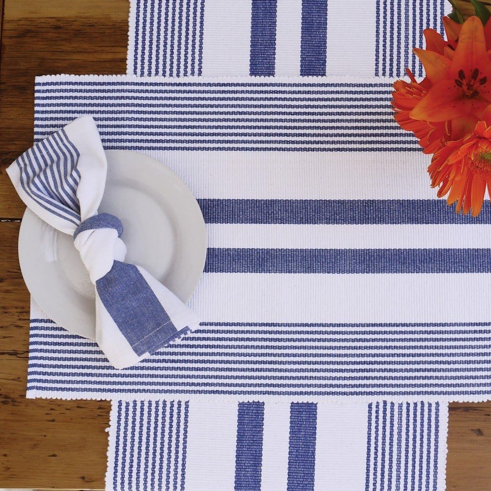 Blue and white striped table runner and placemat with a knotted napkin on a white plate and orange flowers.
