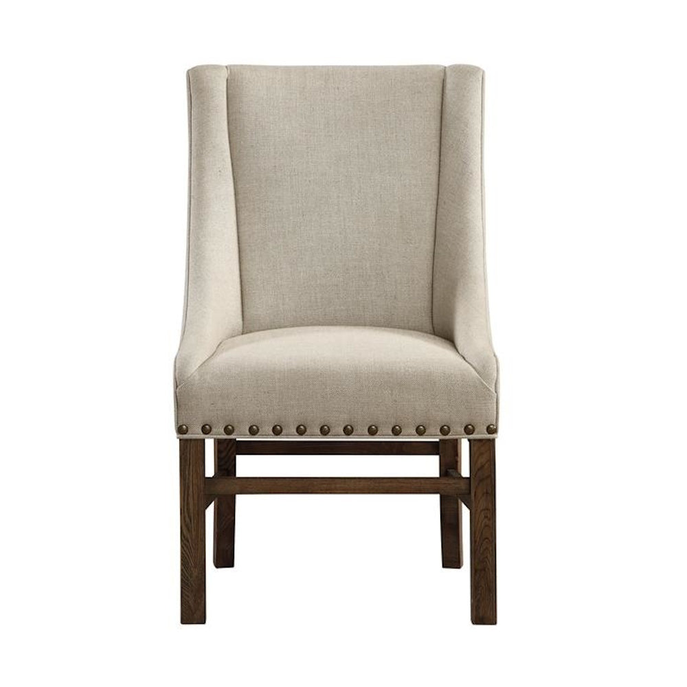 Front view of a beige linen accent chair with nailhead trim and a dark wood base.