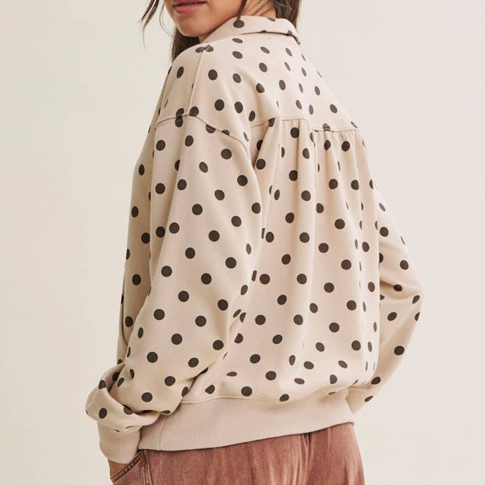 A person wearing a beige pullover with a brown polka dot pattern viewed from the back.