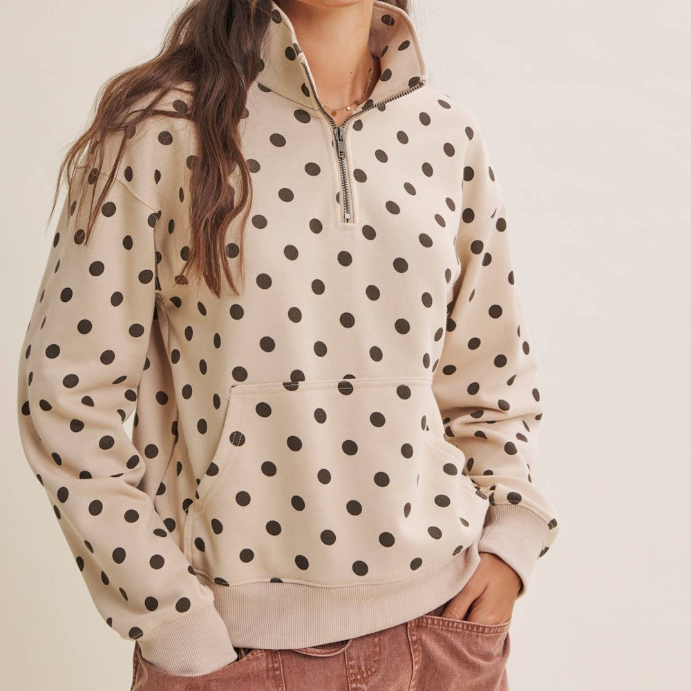 A person wearing a beige half-zip pullover with a brown polka dot pattern and a front pocket.
