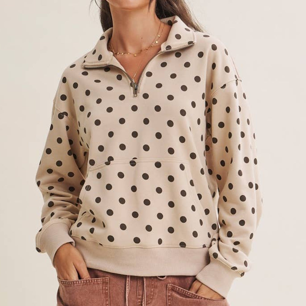 A person wearing a beige half-zip pullover with a brown polka dot pattern and a front pocket.
