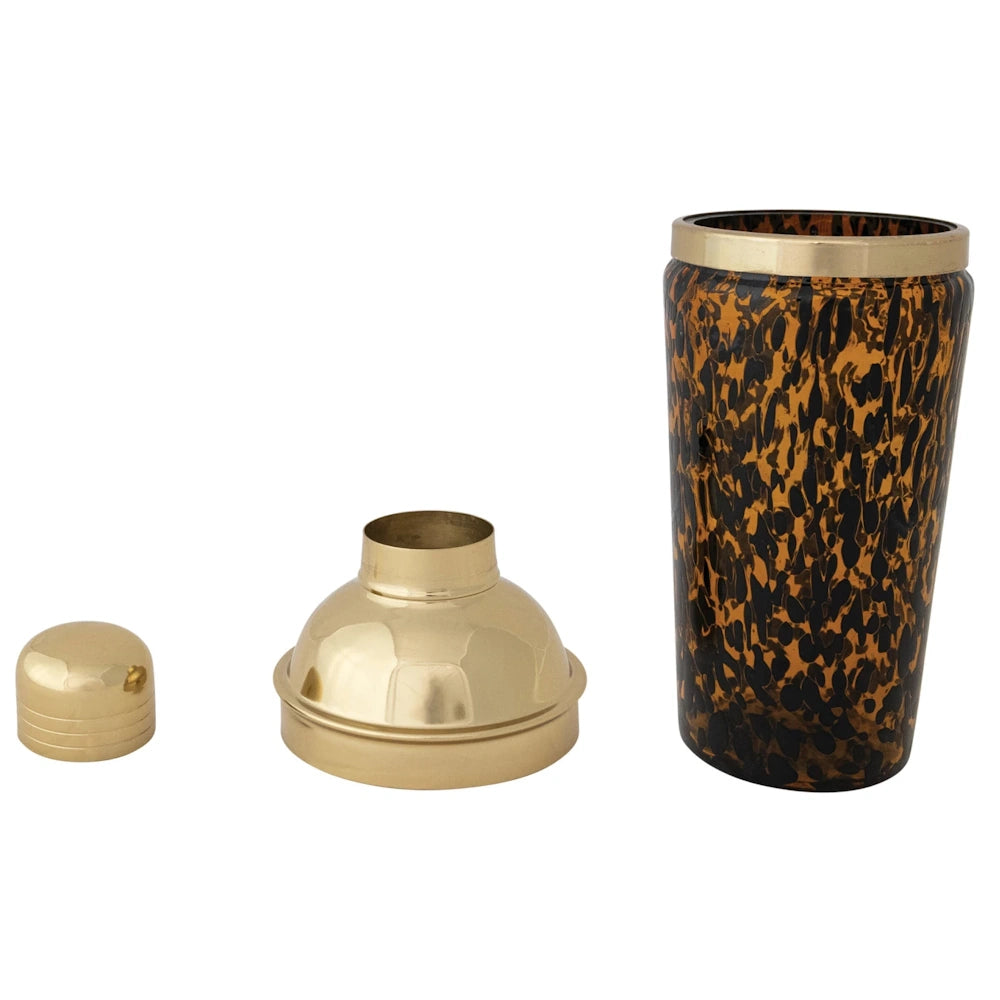 Three-piece tortoise shell glass cocktail shaker with a gold metal strainer lid and jigger cap on a white background.