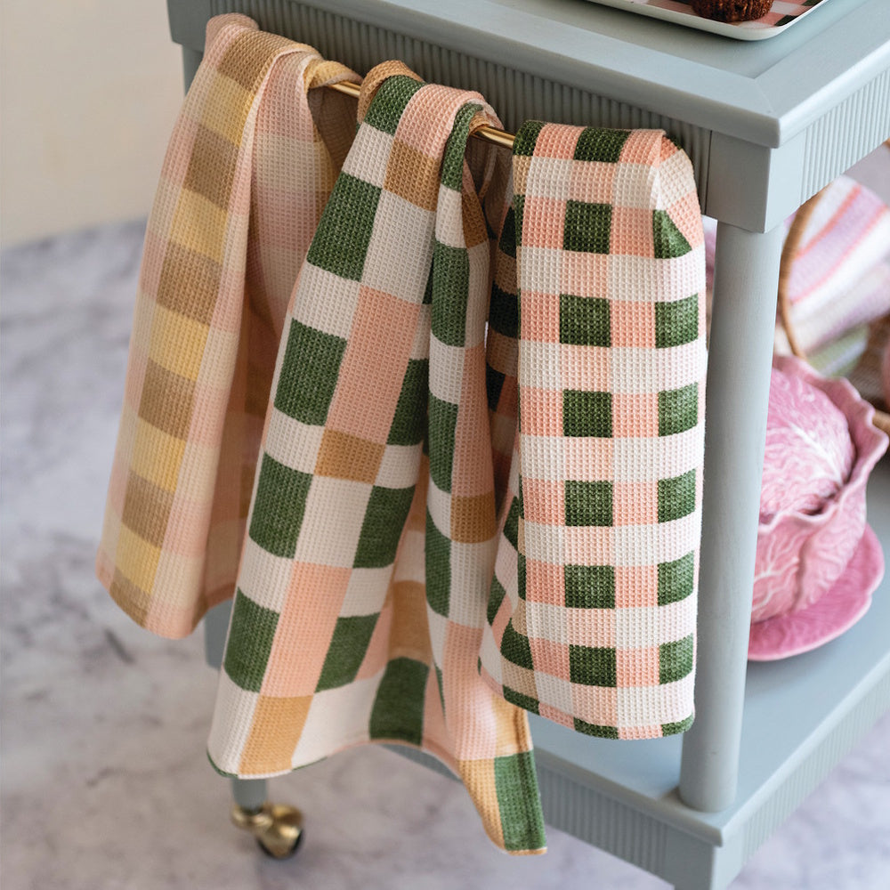 Plaid cotton-blend waffle weave tea towels in peach and green hanging on a light blue kitchen cart.