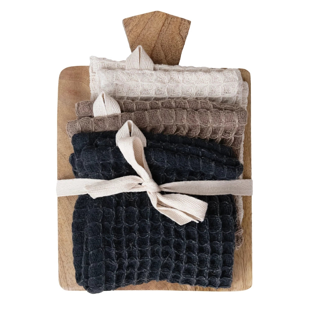 Waffle weave cotton dish cloths in neutral tones tied with a ribbon on a mango wood serving board kitchen gift set.