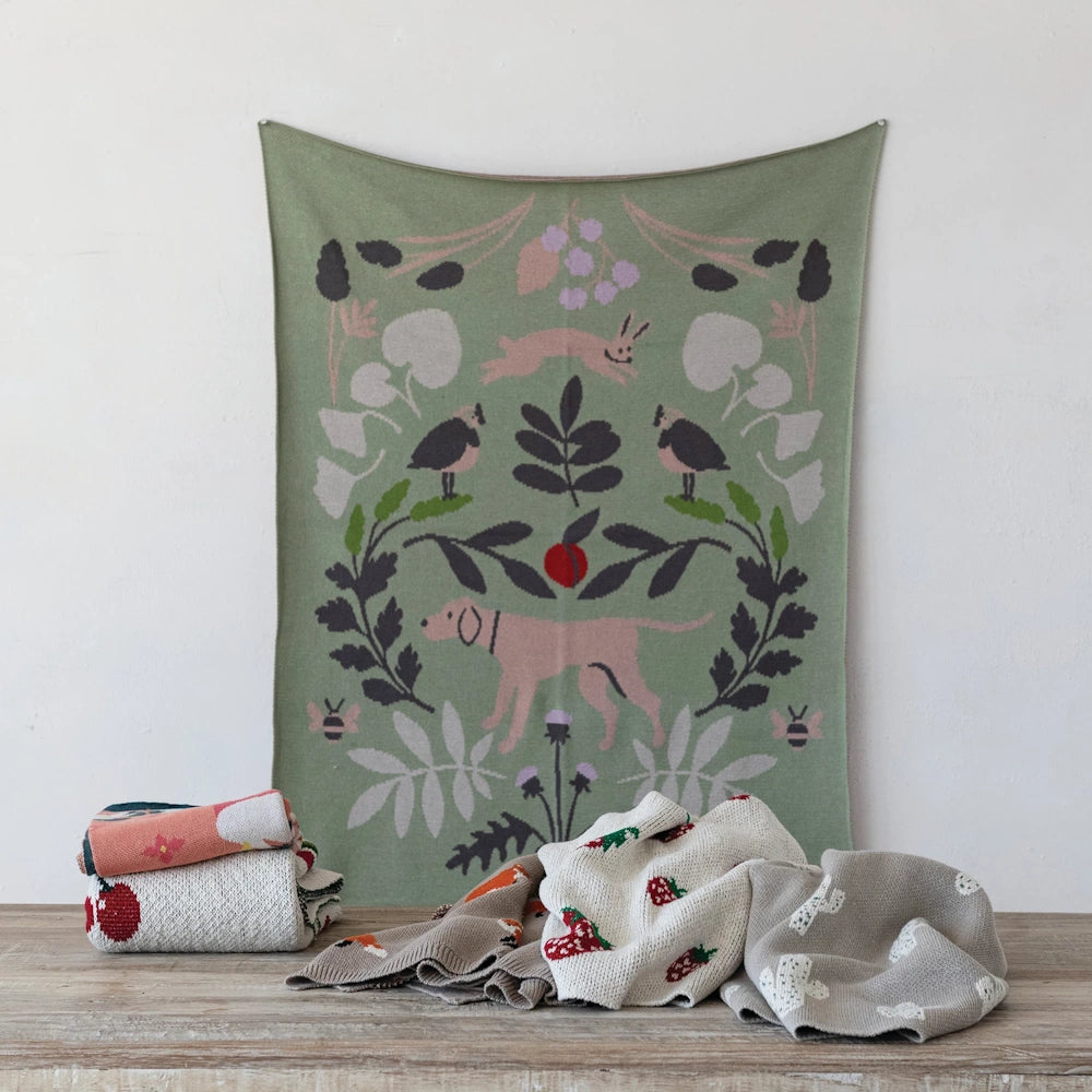 Green knit baby blanket with botanical patterns, a pink dog, rabbit, and birds.